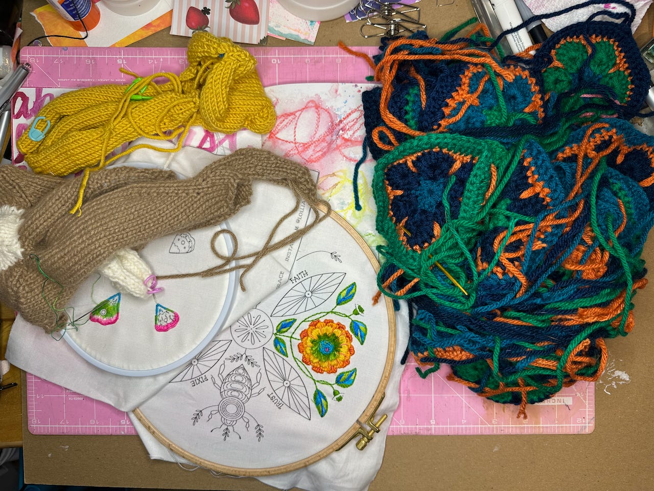 Picture of a pile of craft projects including the partially knit bodies of Pooh and Kanga, two embroidery designs and a stack of crocheted hexagons and pentagons.