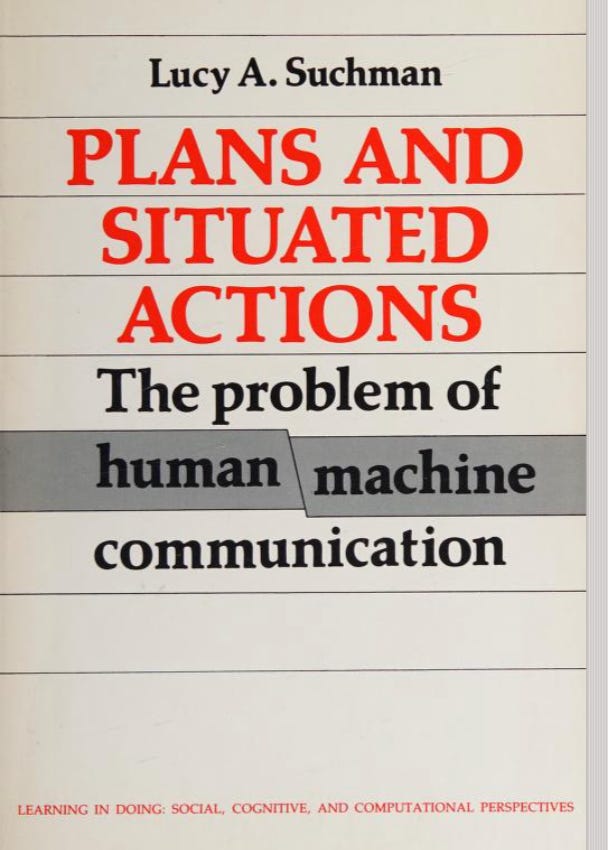 Book cover of Plans and Situated Actions: The Problem of Human-Machine Communication by Lucy A. Suchman, part of the Cambridge University Press series "Learning in Doing: Social, Cognitive, and Computational Perspectives." The cover features a cream background with horizontal lines, the author's name at the top in black, the main title in large red serif type, and the subtitle in black below. The words "human" and "machine" are highlighted with gray bars that meet at an angled break between them, visually evoking the gap between human and machine that the book examines.