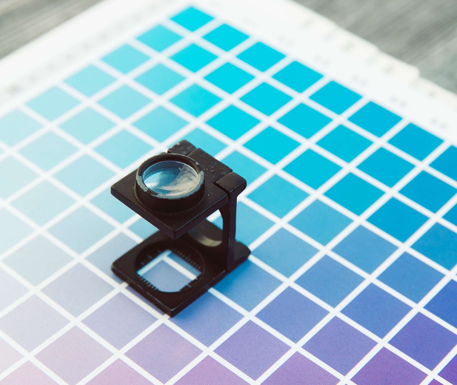Printer’s loupe magnifier tool sitting on a paper with small boxes of varying shads of blue to purple. Printer’s loupe magnifier tool sitting on a paper with small boxes of varying shads of blue to purple.