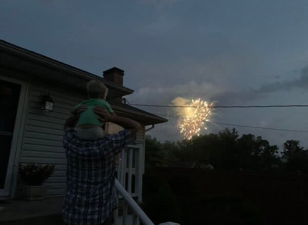 The author’s son sitting on the shoulders of the author’s father. They are looking at a fireworks display bursting in the sky.