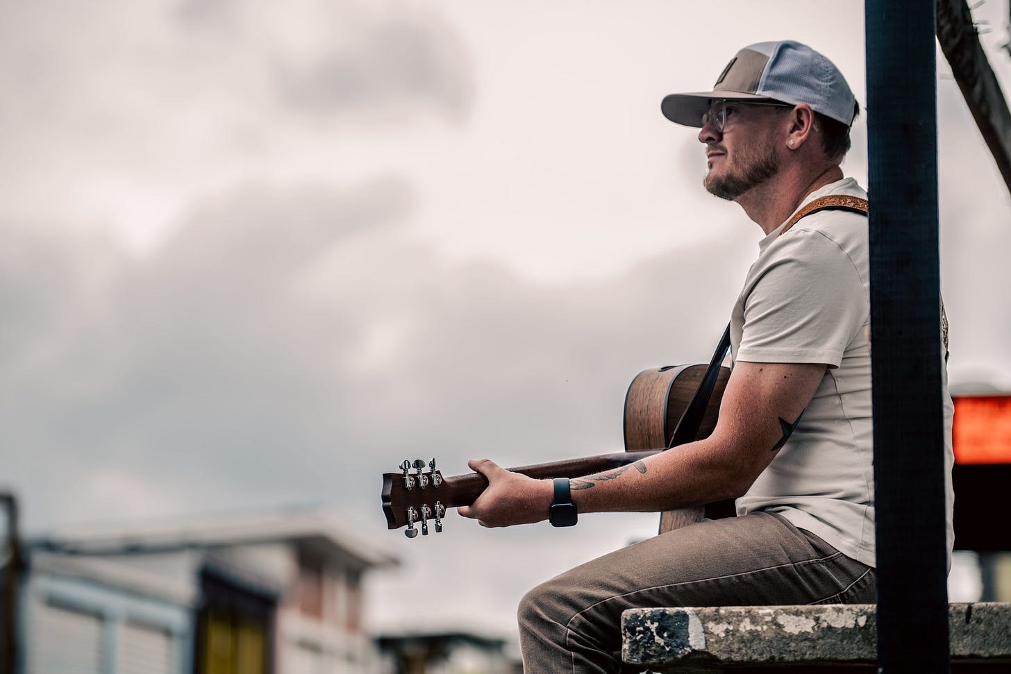Caleb Wolfe, a recording artist from North Carolina, sits on a concrete ledge with his guitar, gazing thoughtfully at the overcast sky. 📸 by Nakeshia Shannon | Shan Media Co. | @ShanMedia.co