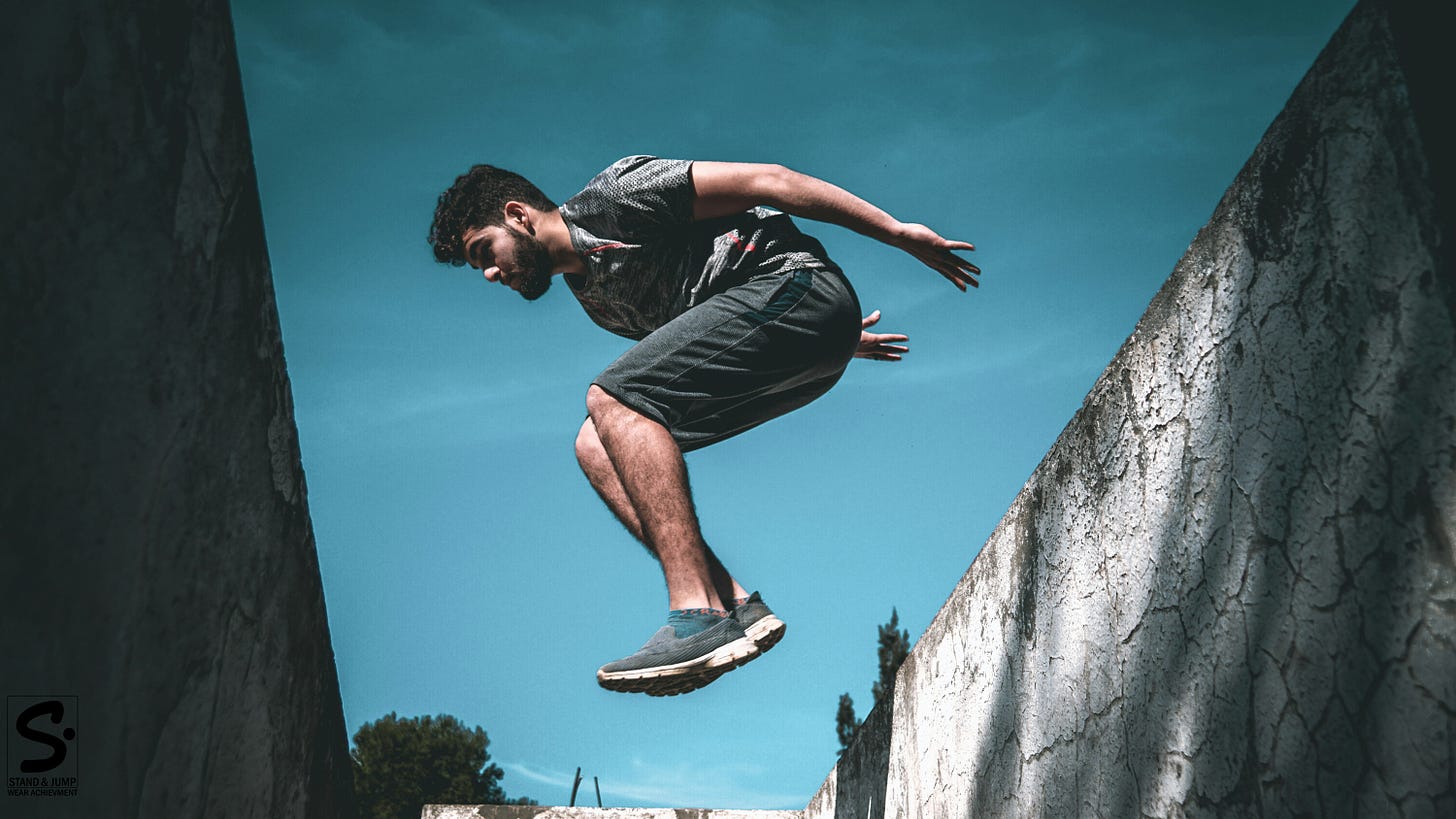 an performing parkour jump between concrete walls against blue sky, demonstrating athletic movement skill for Stand & Jump movement development program