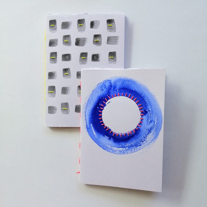 Four watercolour painted handmade notebooks with stitched details.