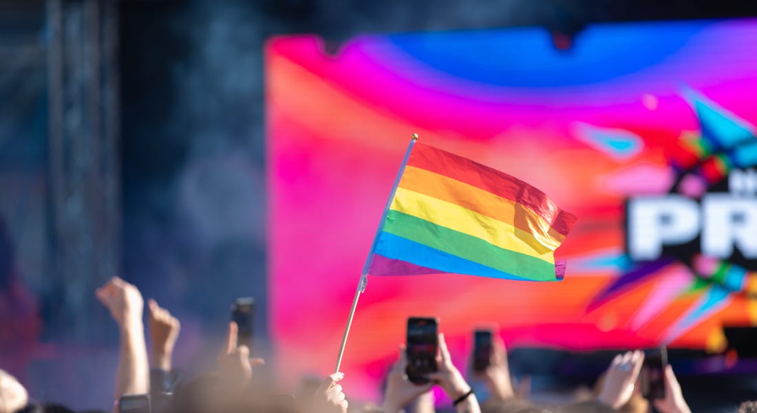 A rainbow flag with a crowd and a rainbow LED board on the stage