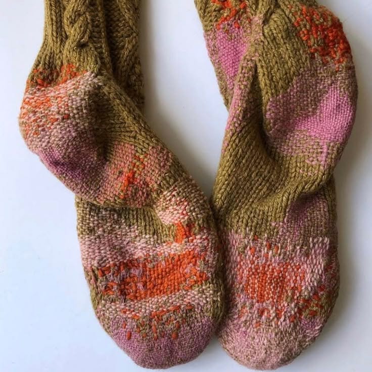 This may contain: two knitted mittens sitting next to each other on a white surface, one with pink and orange designs