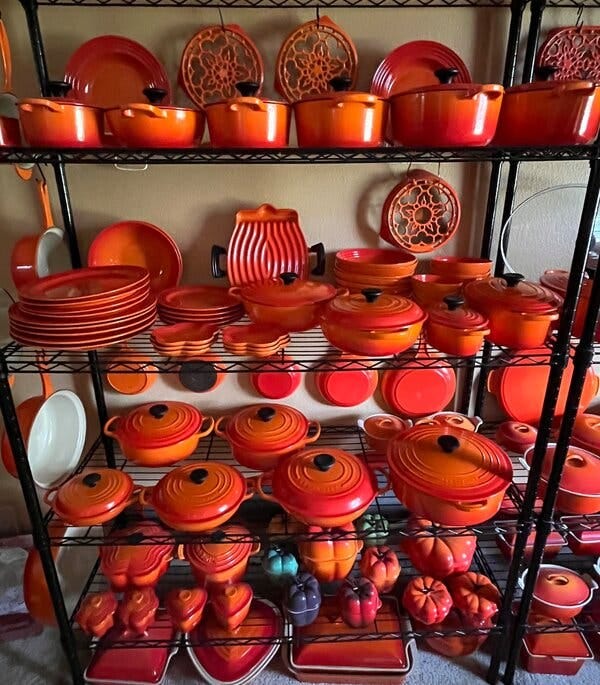 Industrial shelving filled with orange Le Creuset pots, pans, plates, trivets and more. Industrial shelving filled with orange Le Creuset pots, pans, plates, trivets and more.