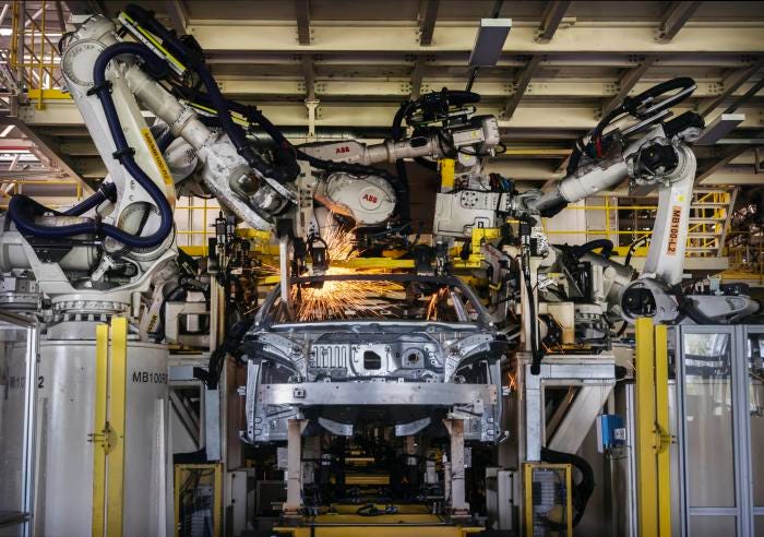 Robotic arms welding parts on the body of an electric vehicle in a factory.