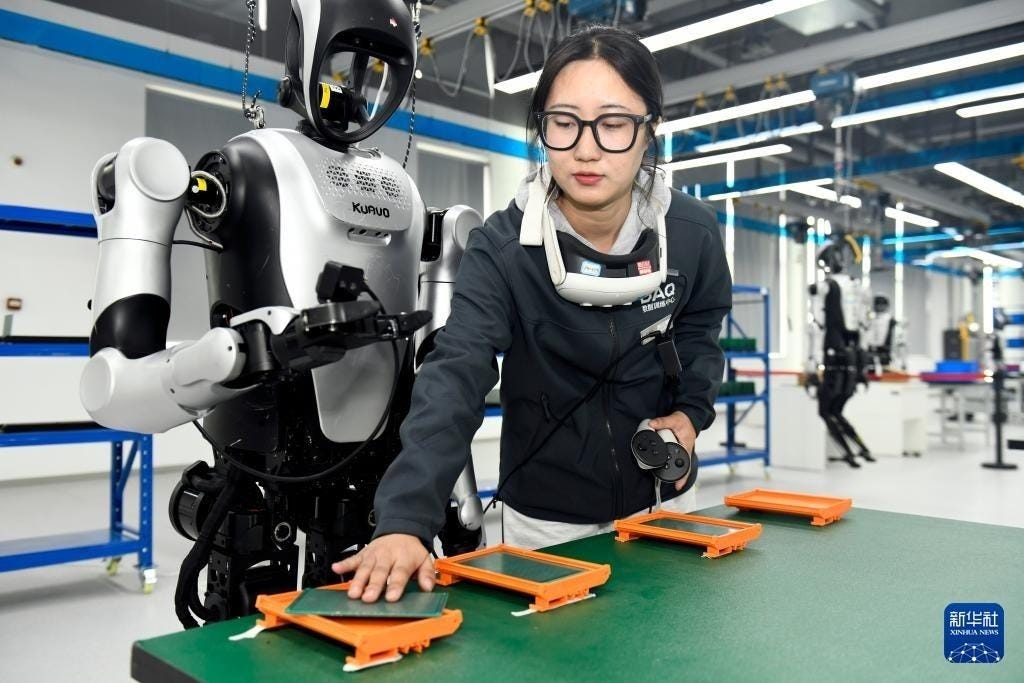 A trainer in a VR headset guides a humanoid through a task at a robot data-collection center in Shandong province in 2026, while its movements are recorded as training data.