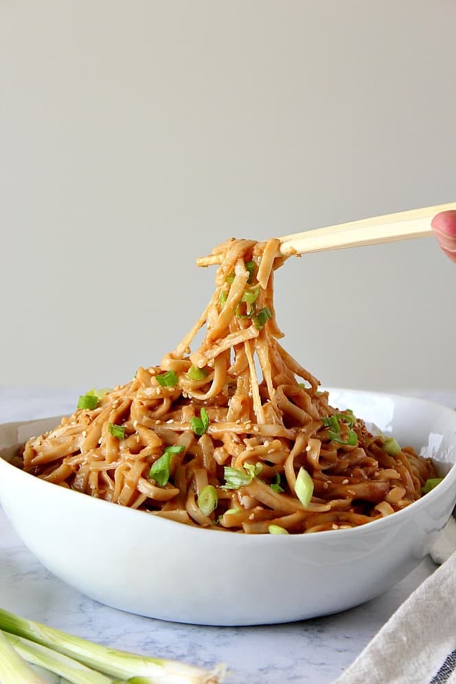 Side shot of white bowl filled with peanut noodles lifted by chopsticks. Side shot of white bowl filled with peanut noodles lifted by chopsticks.