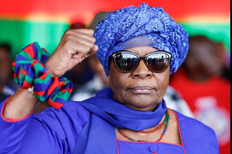 A woman wearing a turban and sunglasses raises her right hand in a black power salute