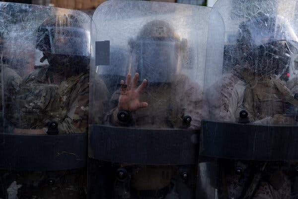 A photo shows people in military gear behind clear shields.