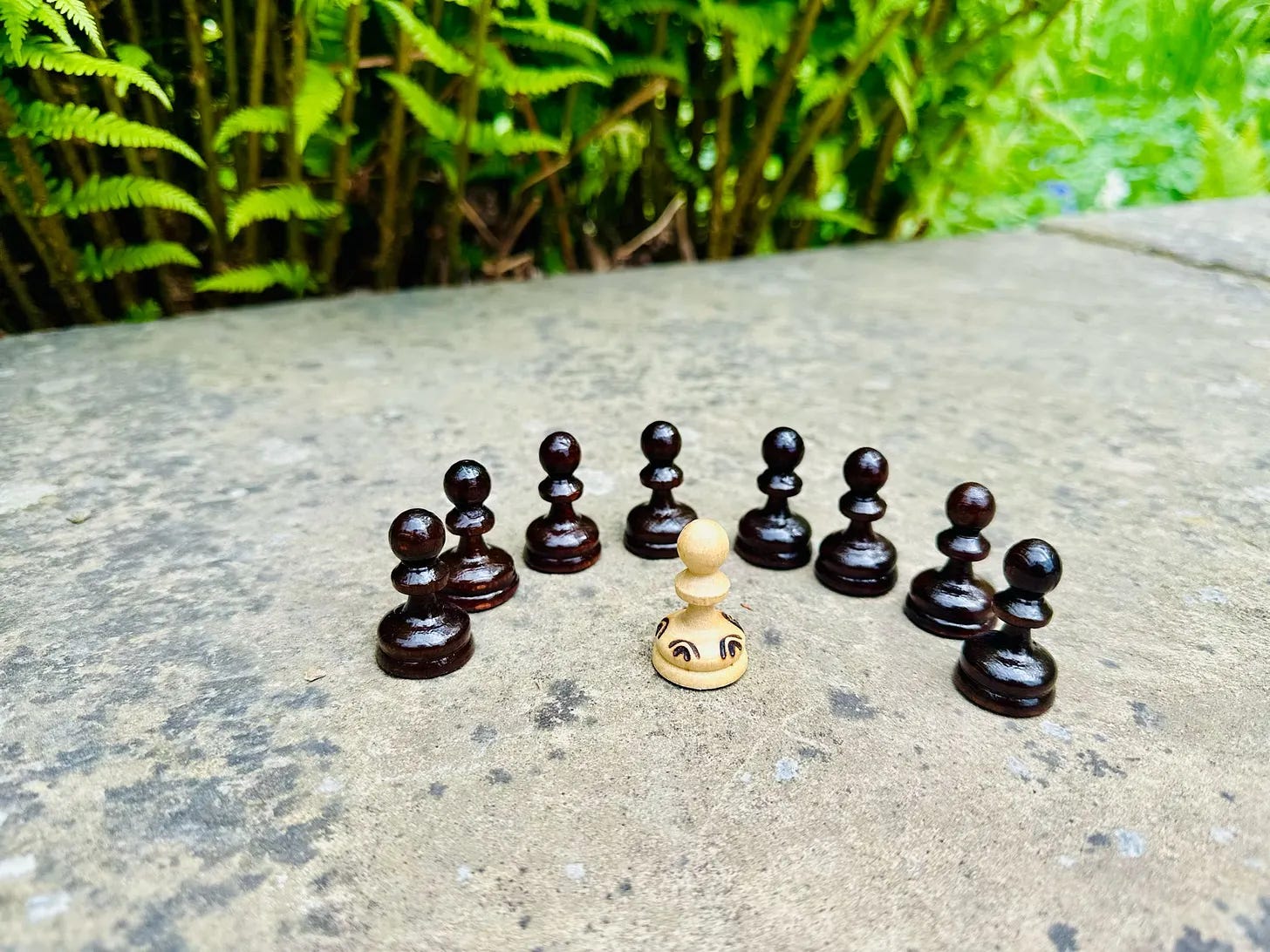 A single chess piece standing alone surrounded by other pieces on a wooden surface outdoors, symbolizing independent decision making.