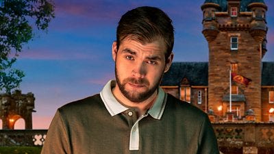 A young man in a polo shirt looks to camera with an eyebrow raised, set against the backdrop of a castle by night A young man in a polo shirt looks to camera with an eyebrow raised, set against the backdrop of a castle by night