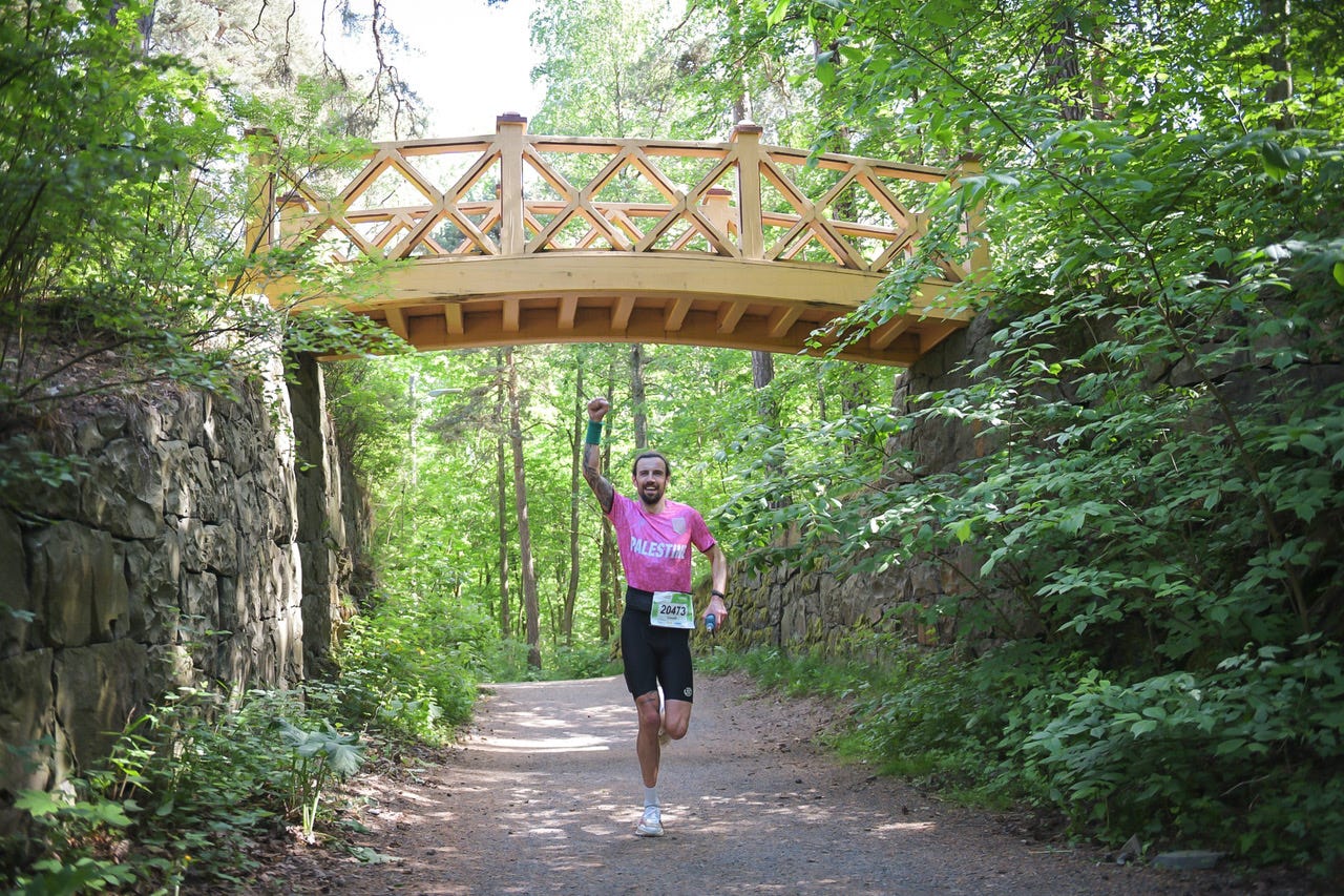 EcoTrail Oslo participant running beneath a wooden bridge on a forest trail EcoTrail Oslo participant running beneath a wooden bridge on a forest trail