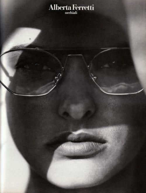 This may contain: a black and white photo of a woman with glasses on her face, looking at the camera