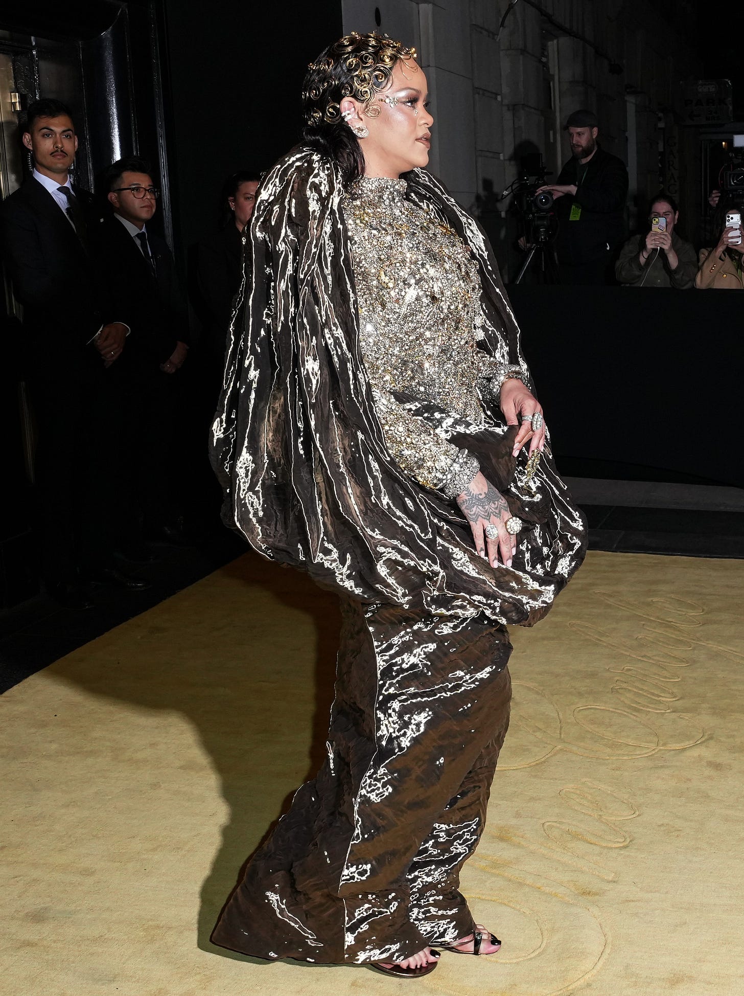 Rihanna wearing a reflective brown and silver Maison Margiela gown, adorned with a sparkling silver top and rings.