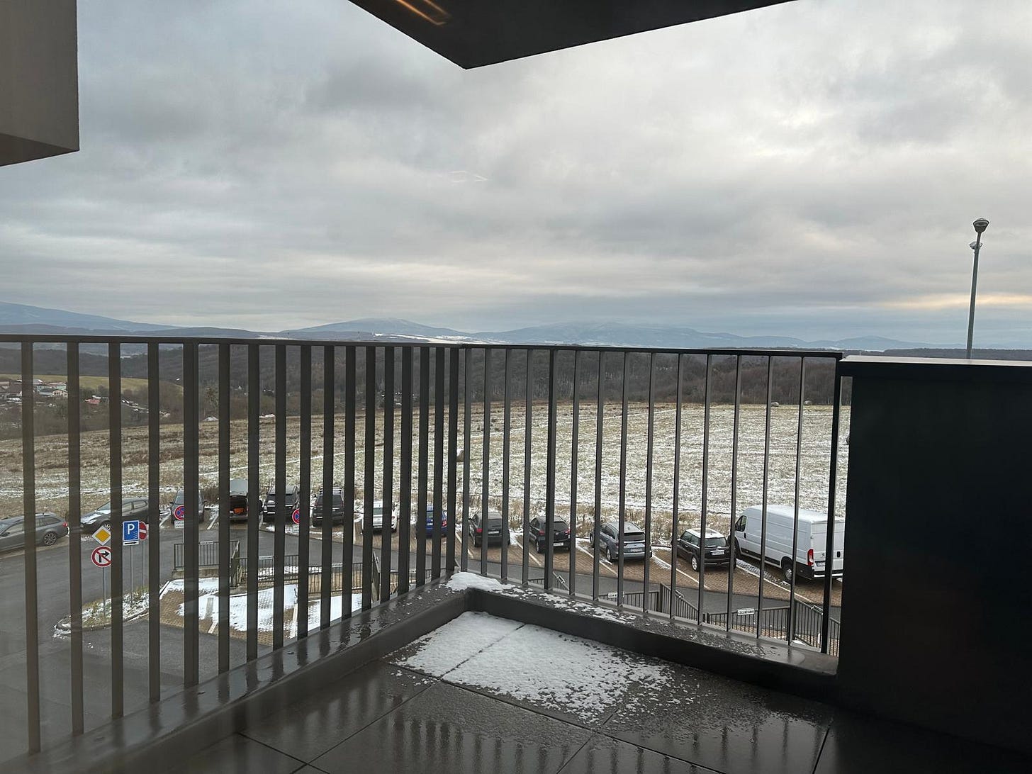 A view from the balcony window of the new apartment showing mountains in the background and a field lightly covered with snow