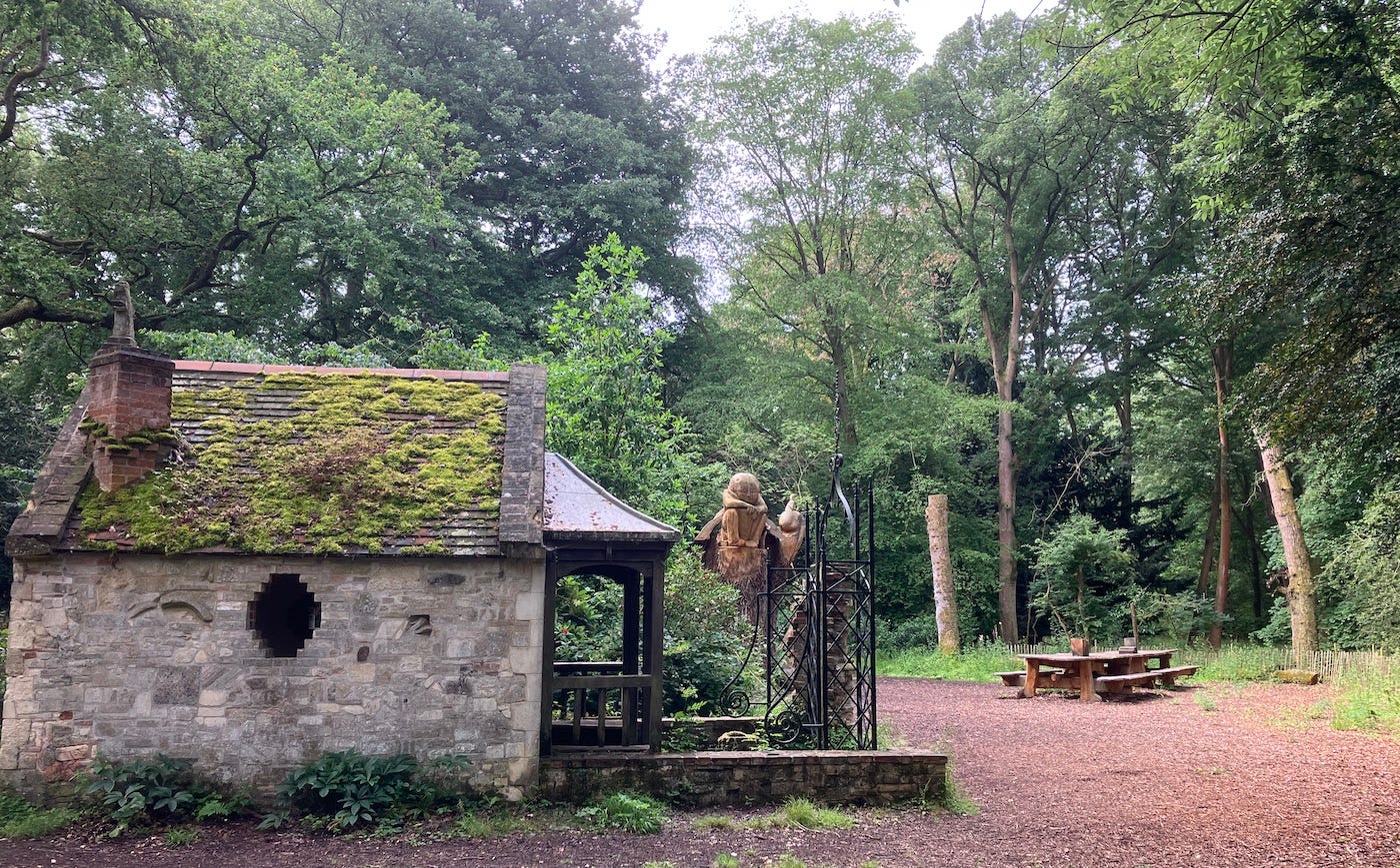 A small building and statue in the woods