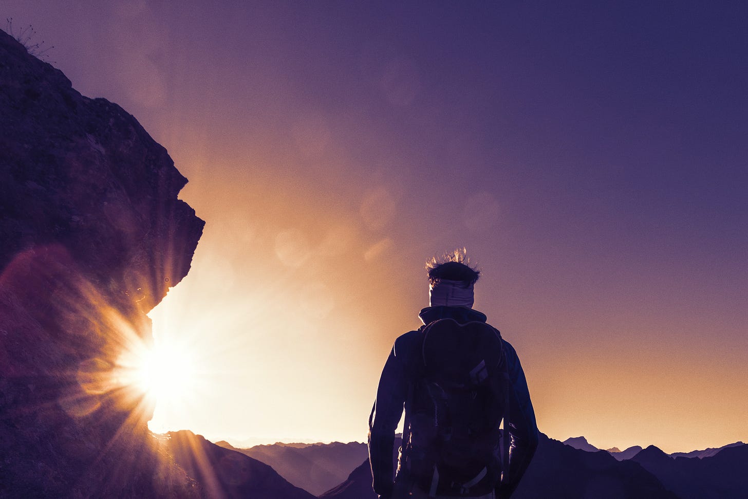 A person standing on a mountain looking toward the sun.