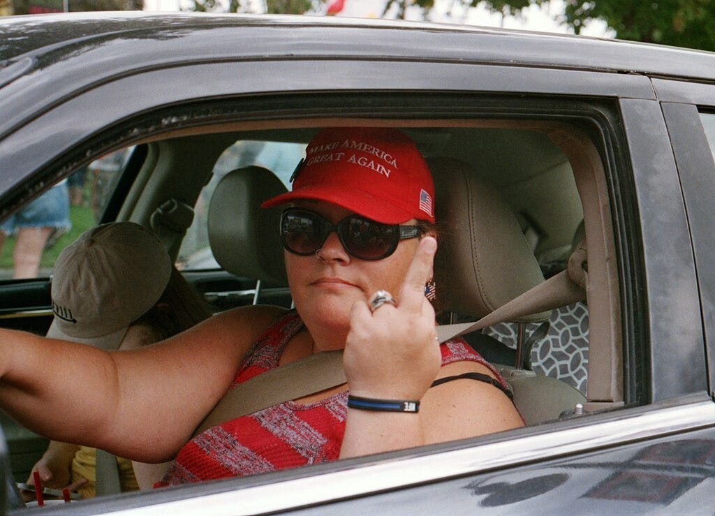 Image of a maga hat wearing woman with raising the middle finger