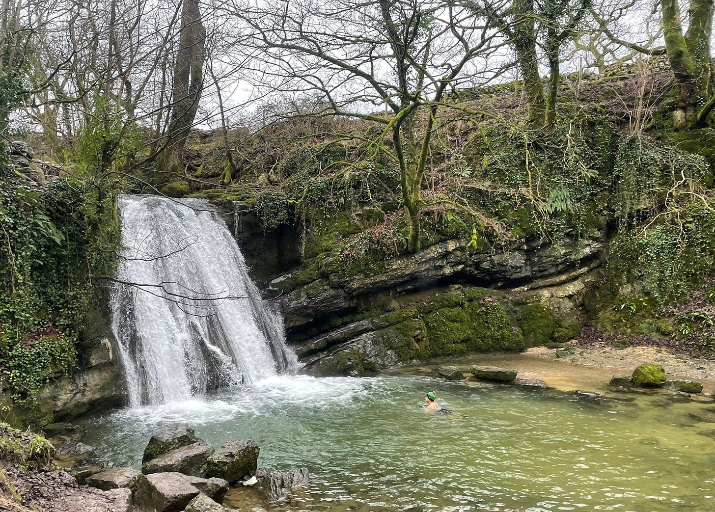 Mixed race woman in a bobble hat swims in the pool beneath a waterfall
