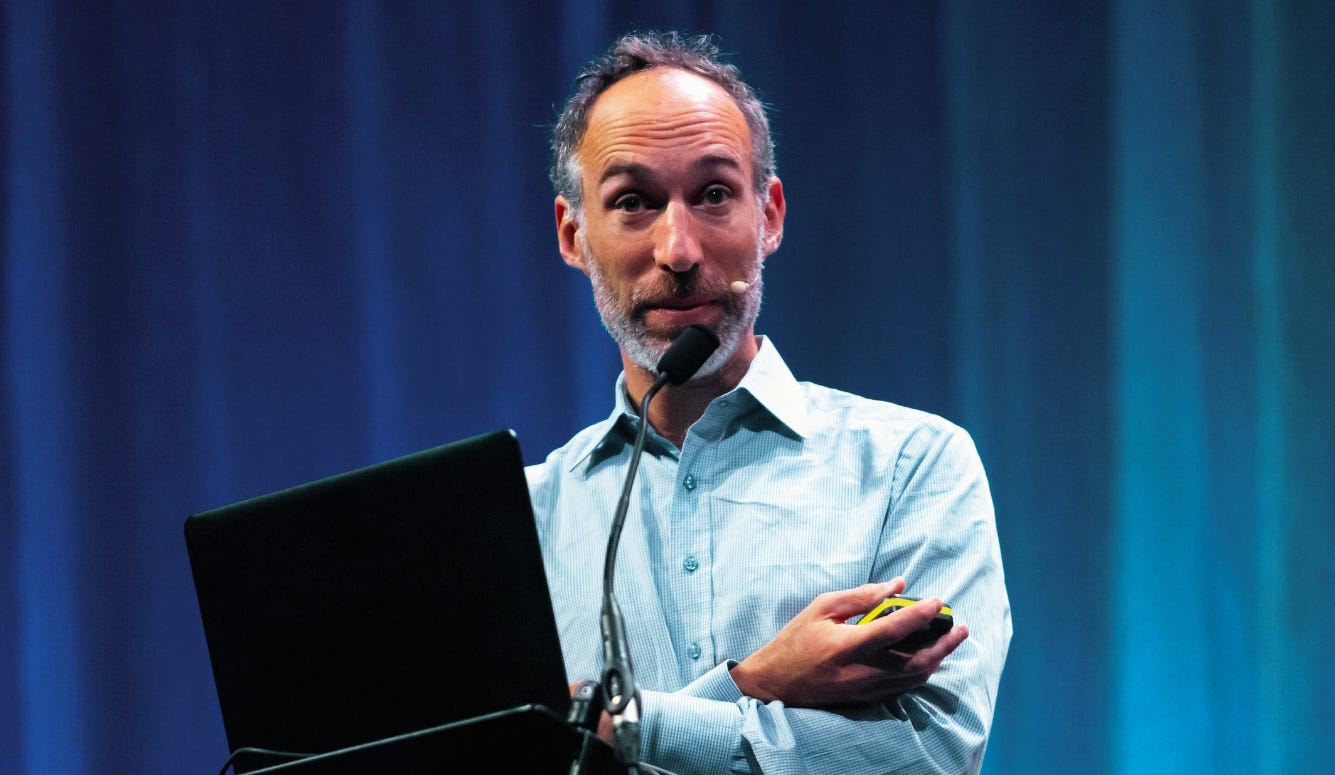 A man holds a laptop on stage while giving a presentation. A man holds a laptop on stage while giving a presentation.