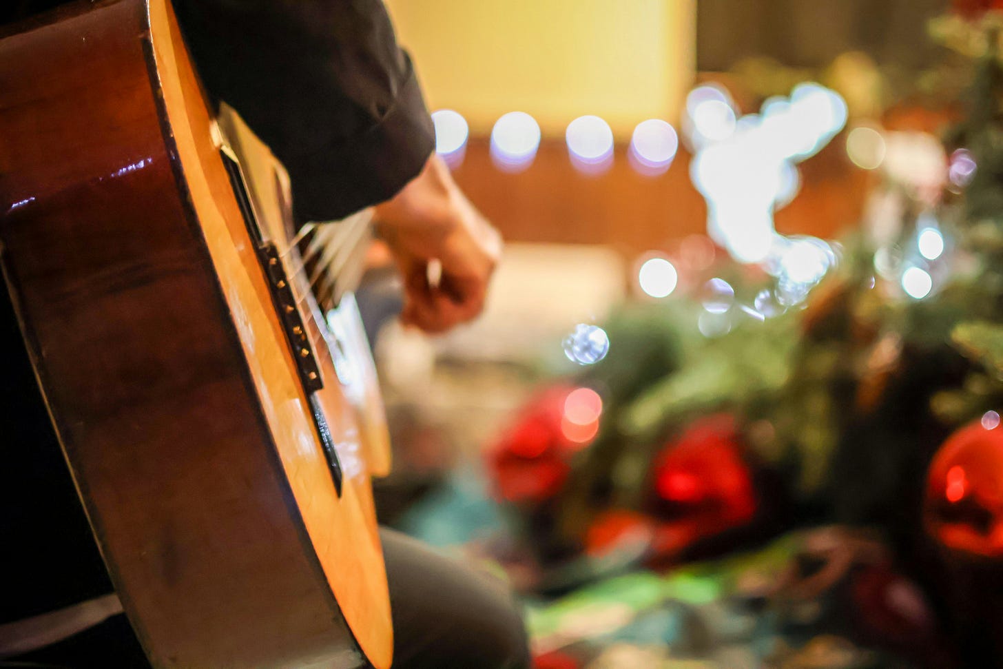 Image of an acoustic guitar being played and a Christmas tree. 