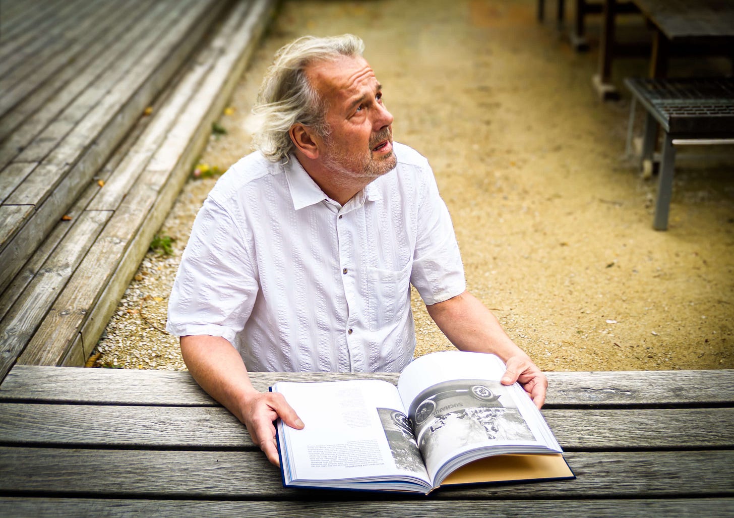 Der Schweizer Autor und Ernährungshistoriker Dominik Flammer sitzt draussen an einem Holztisch und hält sein aufgeschlagenes Buch «Schweizer Schokolade – Alpen, Milch und Pioniere» in den Händen. Er trägt ein weisses Hemd und blickt nachdenklich nach oben. Im Hintergrund sind Holzbänke und ein sandiger Boden zu sehen. Der Schweizer Autor und Ernährungshistoriker Dominik Flammer sitzt draussen an einem Holztisch und hält sein aufgeschlagenes Buch «Schweizer Schokolade – Alpen, Milch und Pioniere» in den Händen. Er trägt ein weisses Hemd und blickt nachdenklich nach oben. Im Hintergrund sind Holzbänke und ein sandiger Boden zu sehen.