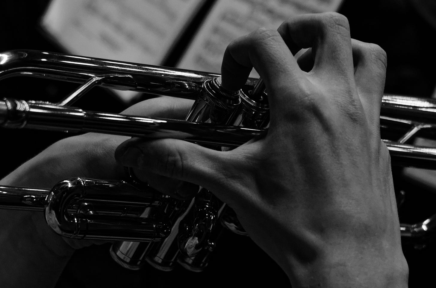 Black-and-white photo of a hand pressing the valves of a trumpet, which is only partly visible. Black-and-white photo of a hand pressing the valves of a trumpet, which is only partly visible.