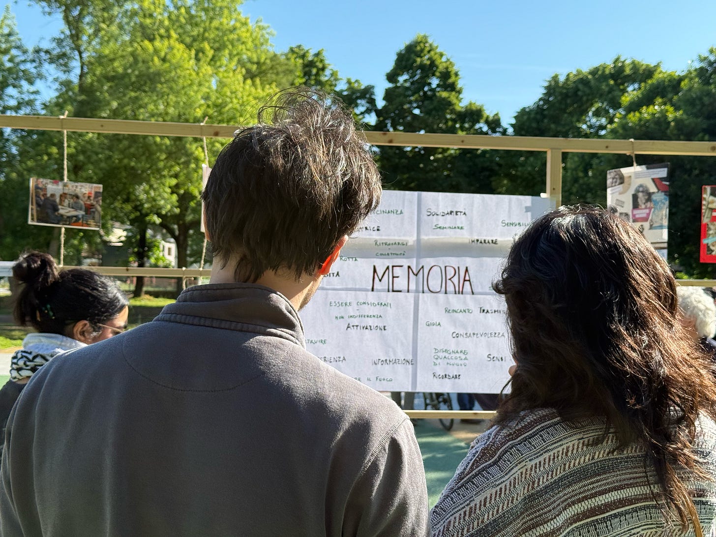 Due partecipanti osservano una parete dedicata alla parola “Memoria”, realizzata durante la mostra fotografica all’aperto del progetto Col.M.A.Te. a Forlì. L’iniziativa, a due anni dall’alluvione del 2023 in Romagna, promuove il ricordo condiviso come strumento di cura e consapevolezza nella crisi climatica.