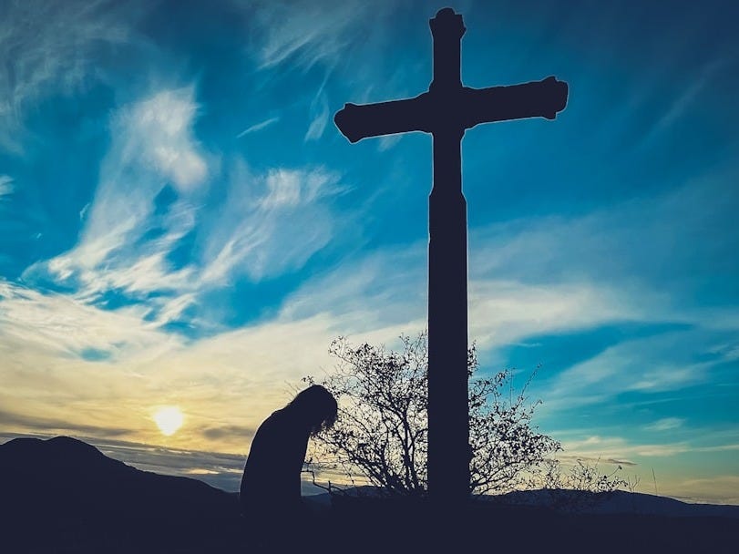 a person kneeling down in front of a cross a person kneeling down in front of a cross