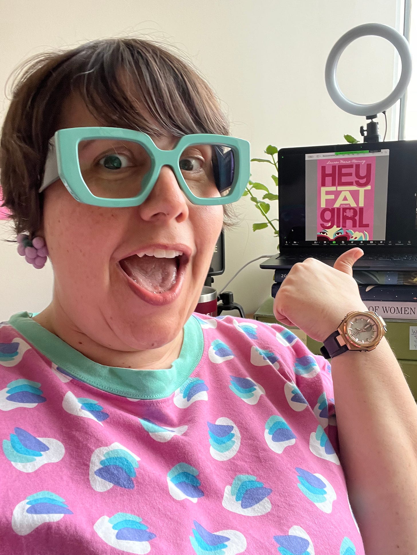 Lauren in a pink and blue shirt pointing to her screen with the pink and blue book cover. Lauren in a pink and blue shirt pointing to her screen with the pink and blue book cover.