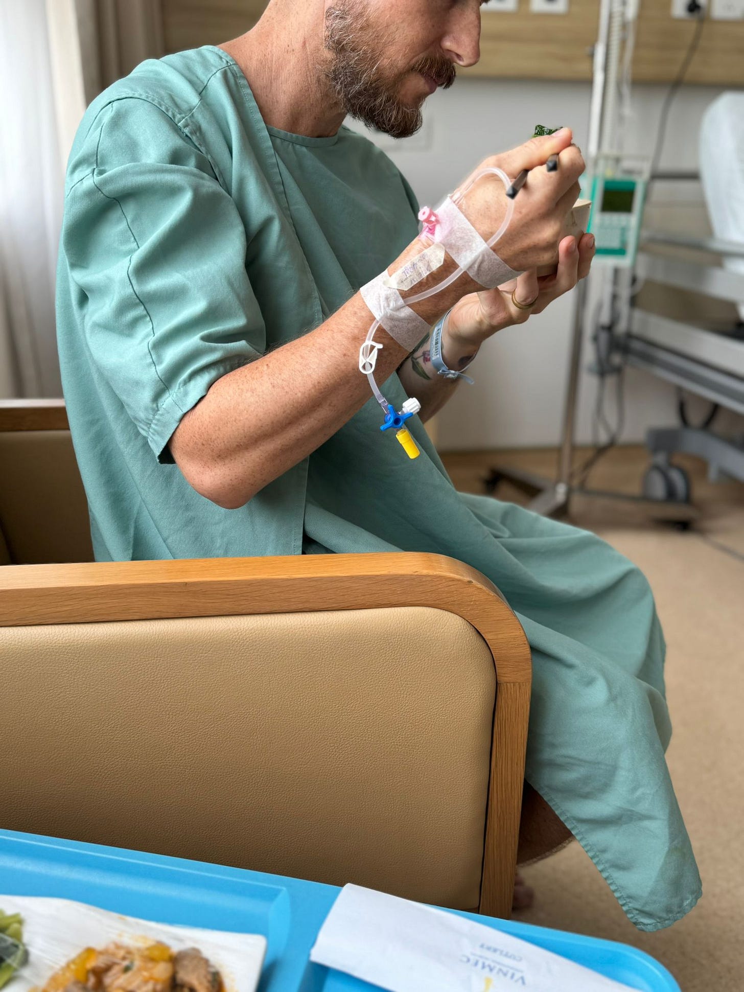 Stephen Belenky in a hospital gown eating lunch after appendix surgery, with an IV in his hand, seated beside a tray of hospital food