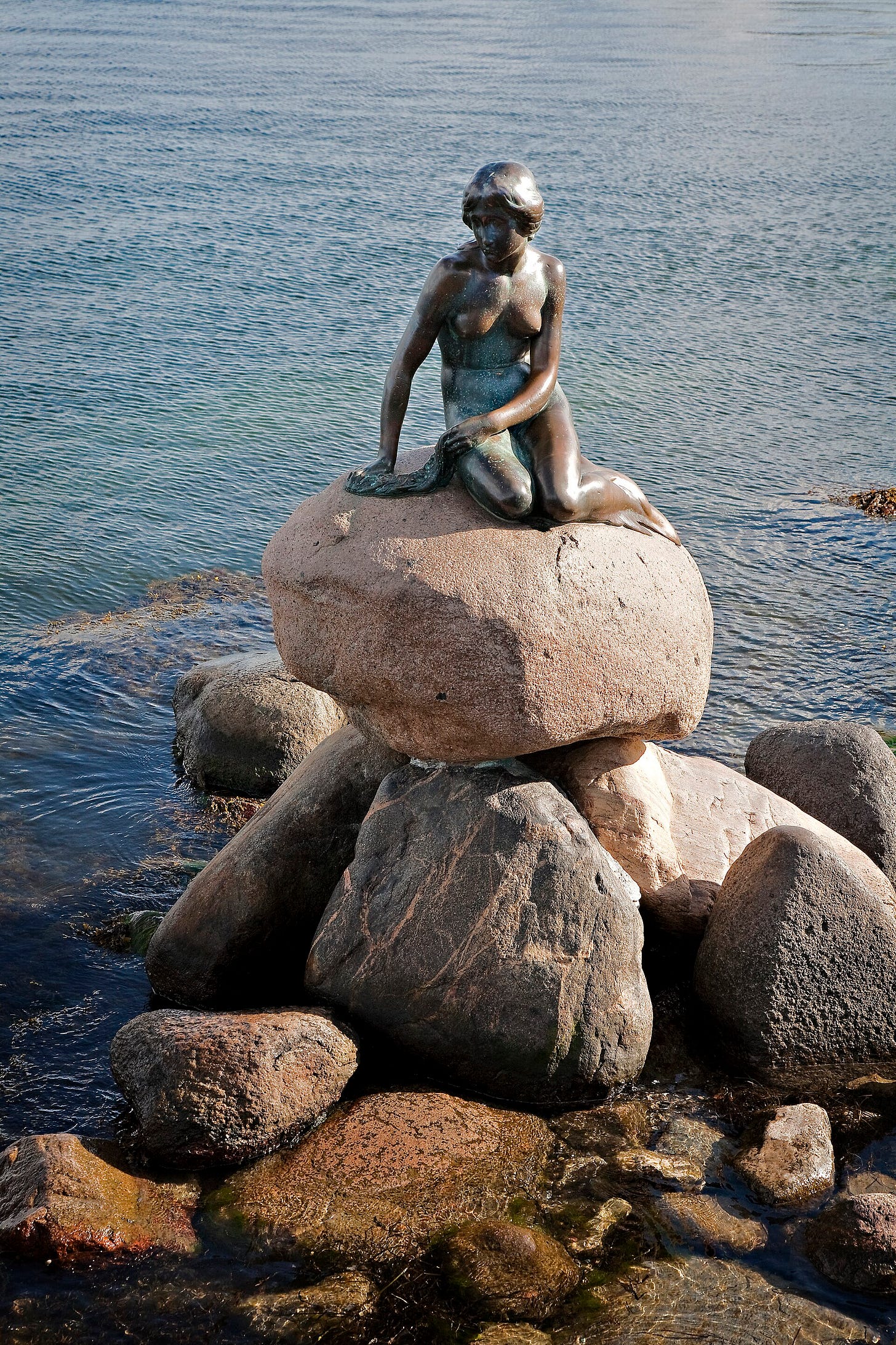 The Little Mermaid by Edvard Eriksen: a small bronze mermaid seated on a granite boulder at the water's edge in Copenhagen The Little Mermaid by Edvard Eriksen: a small bronze mermaid seated on a granite boulder at the water's edge in Copenhagen