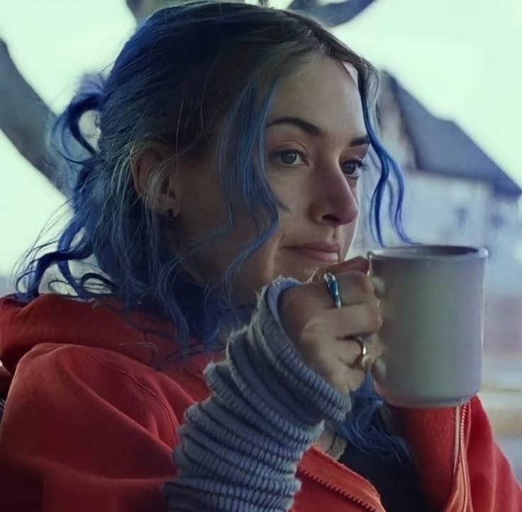 This may contain: a woman with blue hair is holding a coffee cup and looking off into the distance This may contain: a woman with blue hair is holding a coffee cup and looking off into the distance