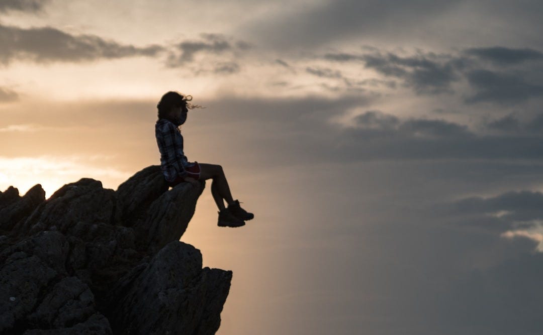 a person sitting on top of a large rock a person sitting on top of a large rock