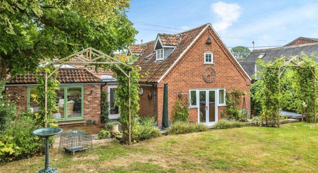 A brown brick house with a green tree, wooden archway, and a lawn outside of it