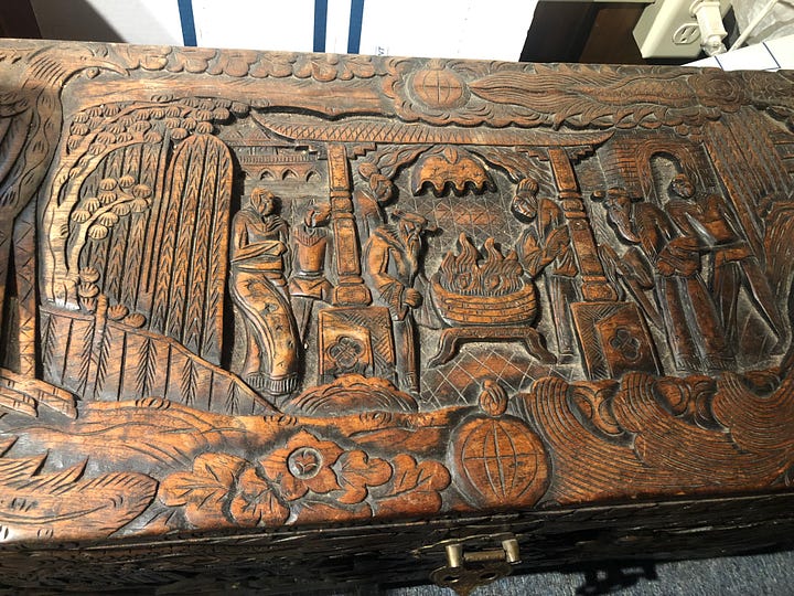 A dark-stained wooden chest ornately carved with images of plants, people, designs and various scenes.