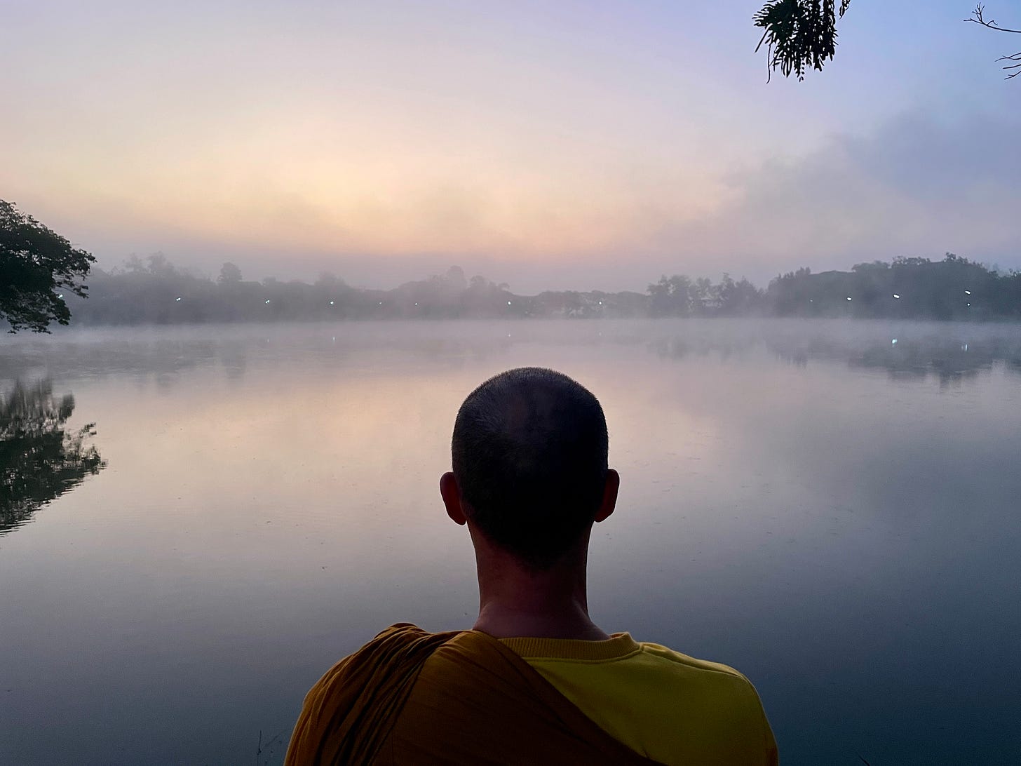 Monk standing in front of a beautiful lake watching the morning mist outside a temple in northern Thailand