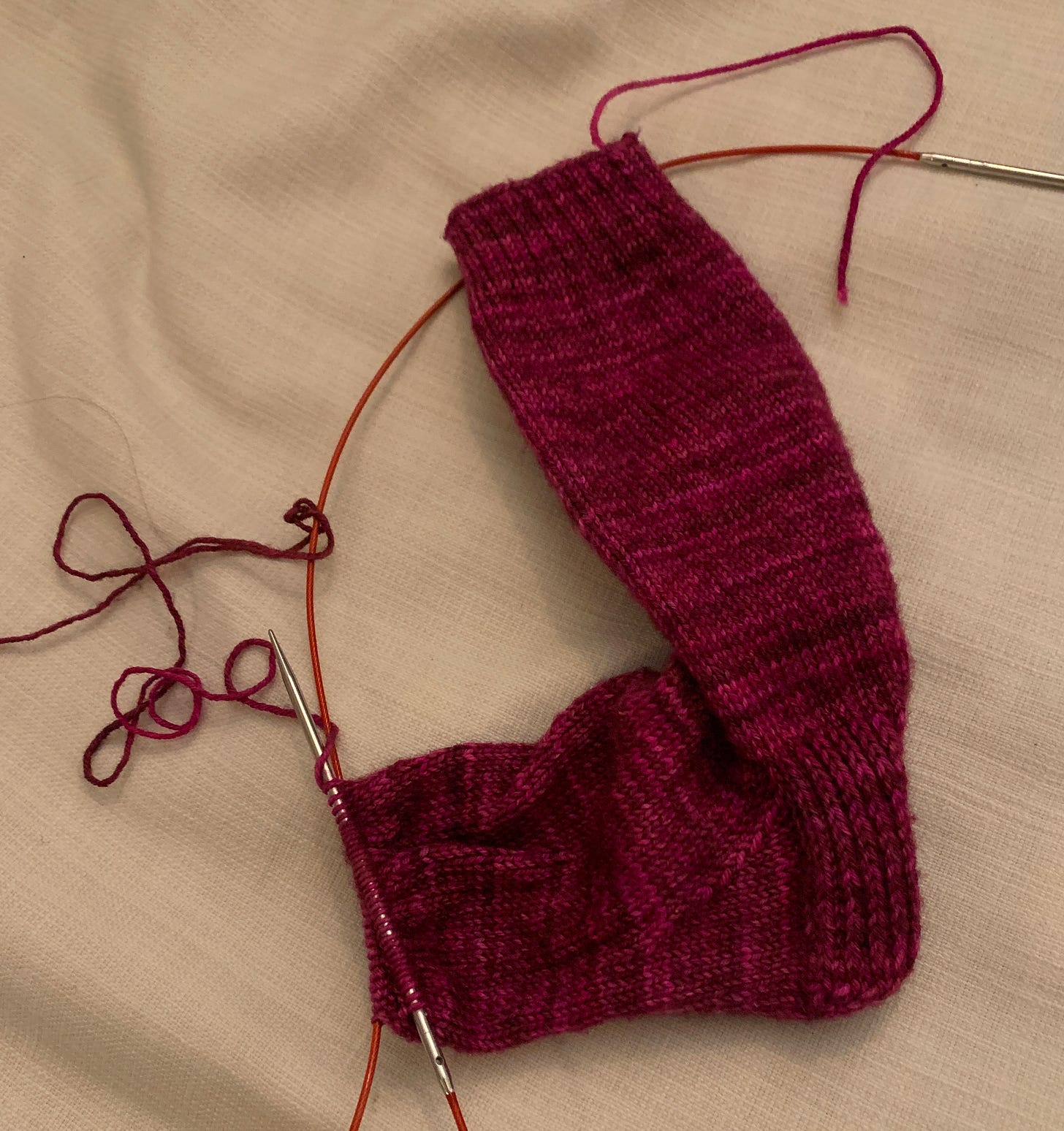 a partially knit pink sock on a pair of circular knitting needles against a white background