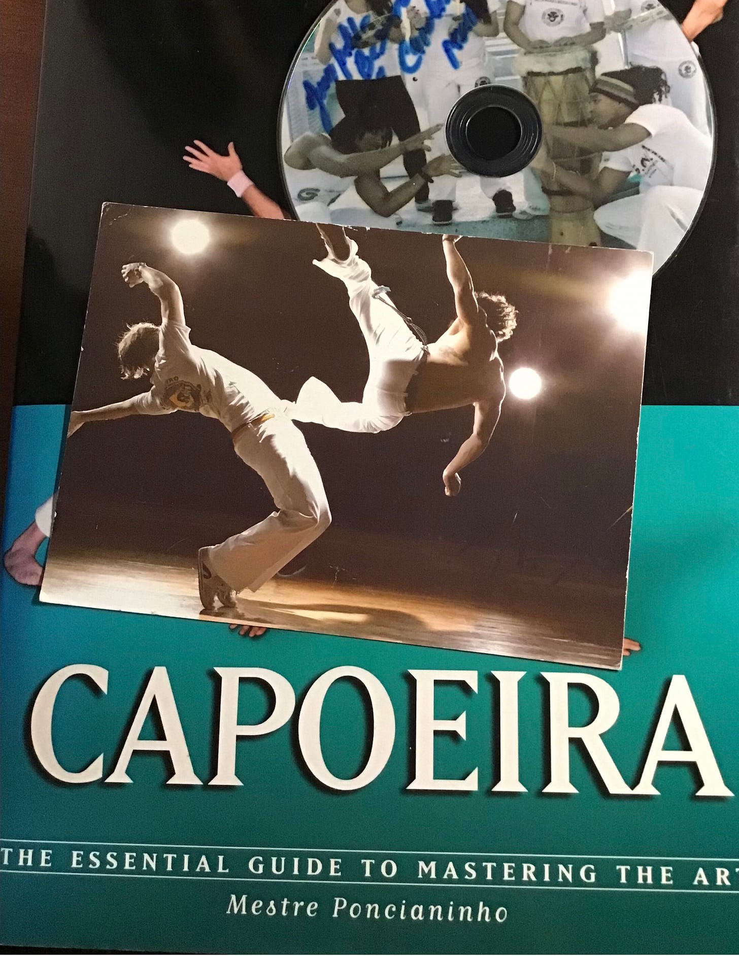 (Arriba, una compilación de canciones de Capoeira hecha por prof. Besouro e instructor Brazil de Nativos de Minas Bogotá. En la mitad, una postal publicitaria de un batizado del grupo Cordao de Ouro Liverpool-Manchester y de fondo, un libro escrito por Mestre Poncianinho que recoge el estilo de Capoeira de Cordão de Ouro) (Arriba, una compilación de canciones de Capoeira hecha por prof. Besouro e instructor Brazil de Nativos de Minas Bogotá. En la mitad, una postal publicitaria de un batizado del grupo Cordao de Ouro Liverpool-Manchester y de fondo, un libro escrito por Mestre Poncianinho que recoge el estilo de Capoeira de Cordão de Ouro)