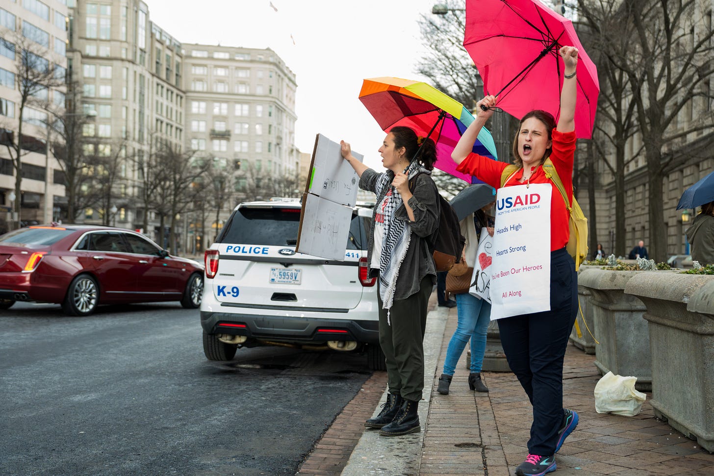Two women with umbrellas hold signs and raise their fists in support of USAID staff in Washington, DC. Two women with umbrellas hold signs and raise their fists in support of USAID staff in Washington, DC.