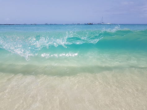 A wooden pier stretching into bright turquoise water, with small waves rolling toward the shore under a clear sky.