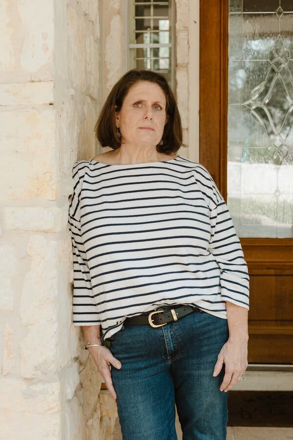 Jennifer Dunn, in a white shirt with blue stripes and jeans, stands in the doorway of a stone building.