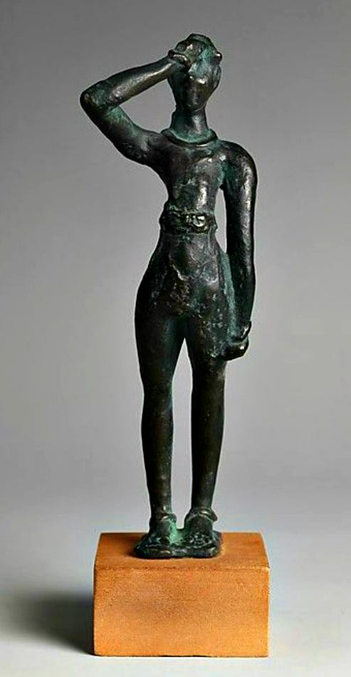 Bronze figurine of a young man performing the Minoan salute. He is standing, facing the camera, holding his right arm up with his right hand loosely curled into a fist against his forehead. He wears a loincloth, a necklace, bracelets, and anklets.