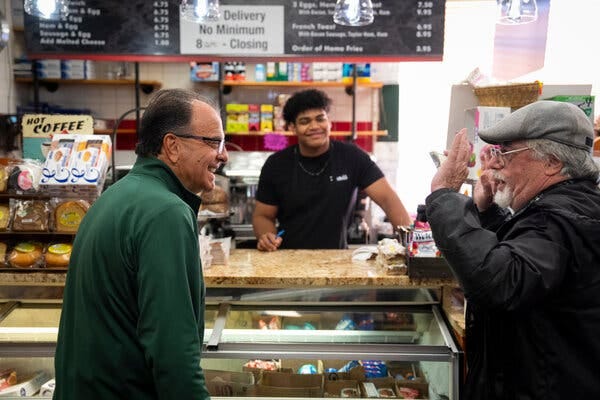 Steve Natoli has a conversation with two other men at a deli, one of whom is behind the counter.