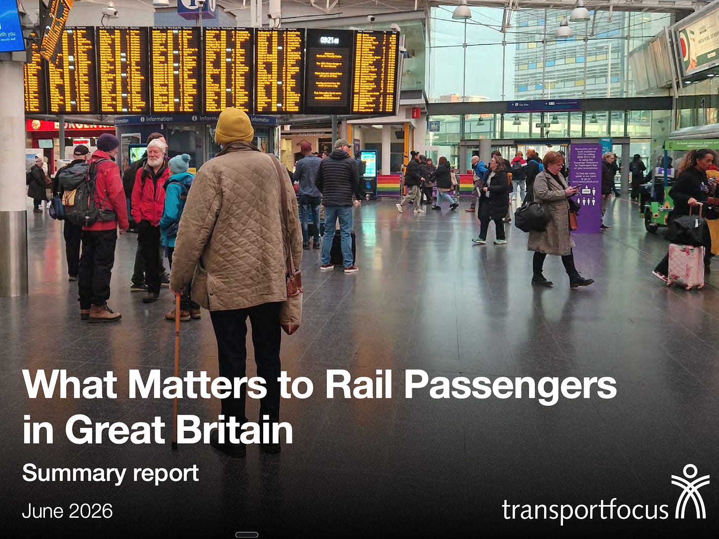 A busy railway station concourse, shot from behind a person in a quilted jacket using a walking stick. Large orange departure boards fill the upper half. Bold white text overlaid reads: "What Matters to Rail Passengers in Great Britain — Summary report, June 2026." Transport Focus logo bottom right.