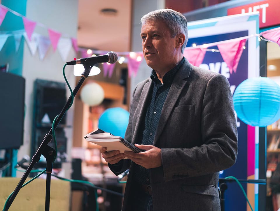 Photo of Jonathan Davidson at a mic reading from a book.