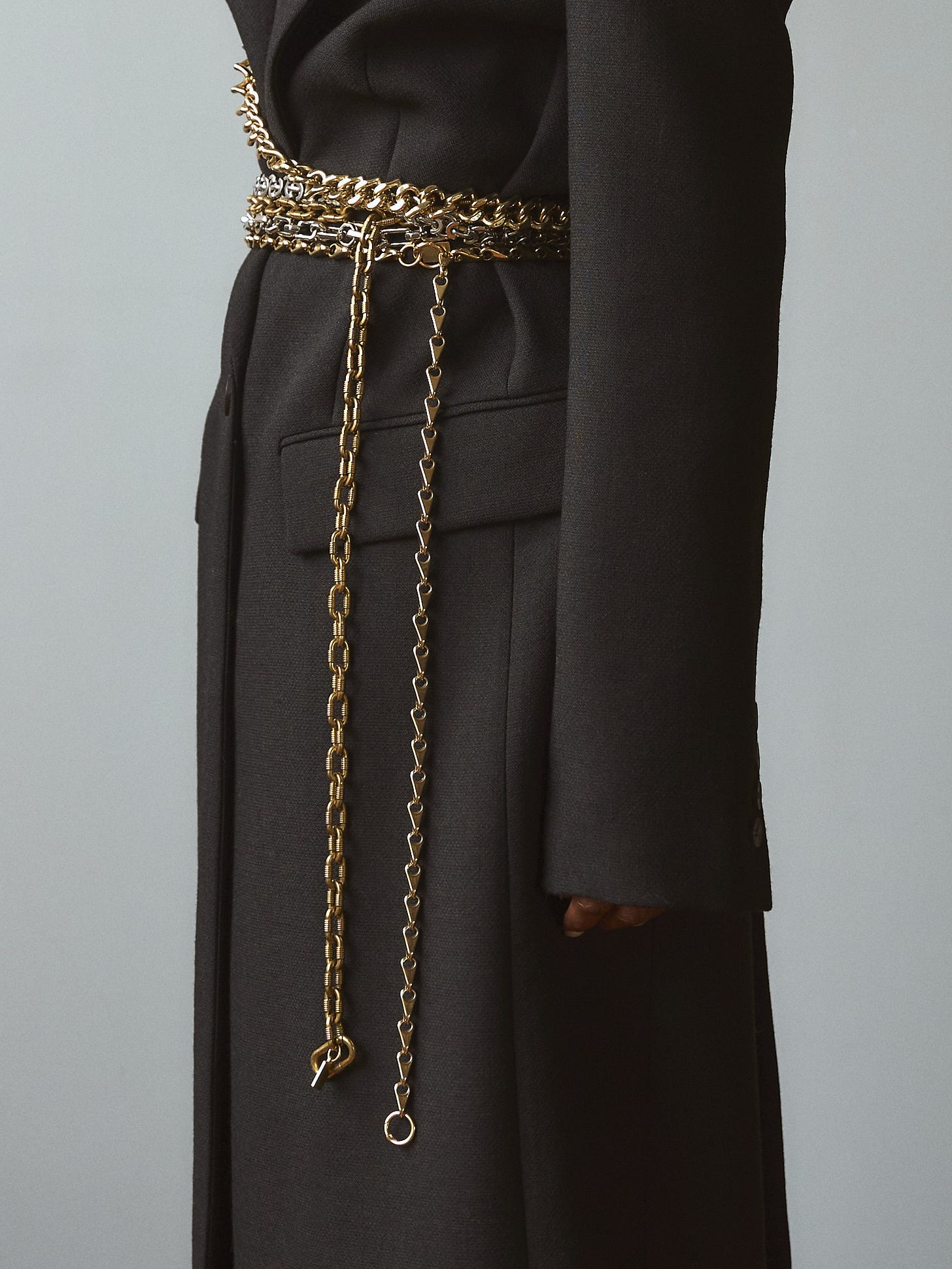 Side view of the Lapo Lounge Eris, Hyperion, Himalia, and Zira chain belts cinched over a minimalist black overcoat.