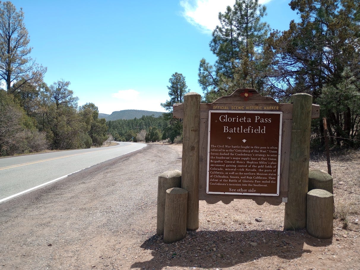 Historical marker on dry ground with trees and mountains in background Historical marker on dry ground with trees and mountains in background